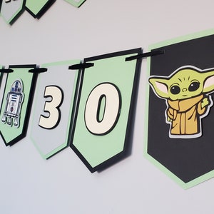 May include: A green, black and white banner with the numbers 30 and a character from Star Wars. The banner is decorated with a black and white image of R2-D2.