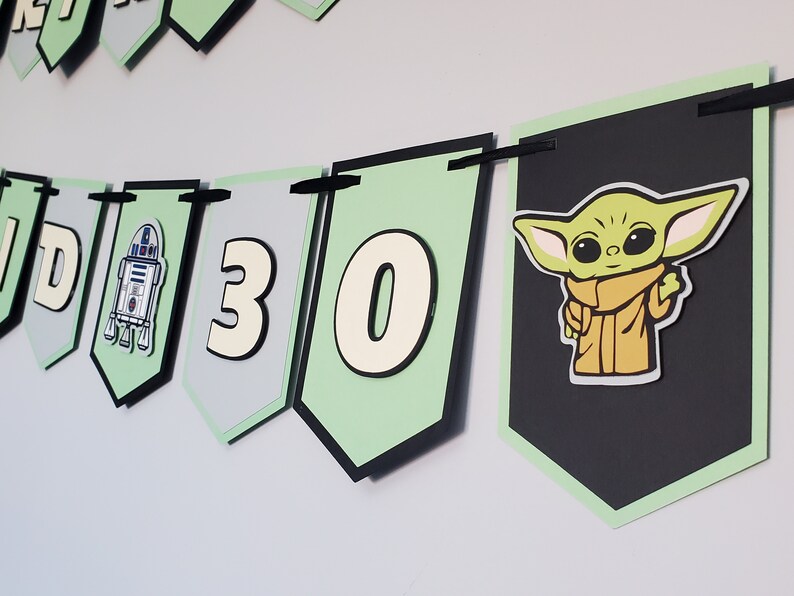 May include: A green, black and white banner with the numbers 30 and a character from Star Wars. The banner is decorated with a black and white image of R2-D2.