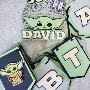 May include: A green and black banner with the letters "DAVID" and the number "30" in white. The banner also features a green character with large ears and a white character with a round body. The banner is decorated with a grey and white image of a Death Star.