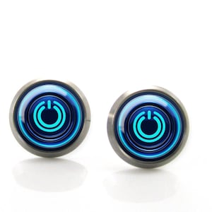 Puede incluir: Un par de gemelos redondos de color plateado con un diseño de botón de encendido azul. El gráfico del botón de encendido es de un azul brillante y brillante sobre un fondo azul oscuro. Sobre un fondo blanco.