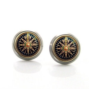 Puede incluir: Un par de pendientes de botón de plata con un diseño de brújula. La brújula tiene un fondo negro con detalles dorados y un centro rojo.