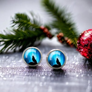 Puede incluir: Un par de pendientes de botón plateados con una imagen azul y blanca de un lobo aullando a la luna.