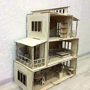Pu&ograve; includere: Una casa delle bambole in legno con pi&ugrave; livelli e stanze, tra cui un balcone, finestre e una porta. La casa delle bambole &egrave; realizzata in legno chiaro e ha un design semplice e moderno.