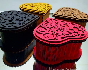 May include: Four heart-shaped wooden boxes with intricate laser-cut designs. The boxes are painted in red, black, brown, and yellow. The boxes are arranged on a reflective surface. The text "HobbyLaserDesignArt" is visible in the lower right corner of the image. The image also includes icons for the following file formats: CDR, DXF, SVG, AI, and PDF.