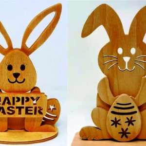 May include: Two wooden Easter bunny decorations. The bunny on the left is holding a sign that says "Happy Easter". The bunny on the right is holding an egg.