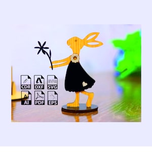 May include: A wooden cutout of a rabbit holding a flower. The rabbit is wearing a black dress and has a heart on its chest. The rabbit is standing on a wooden base.