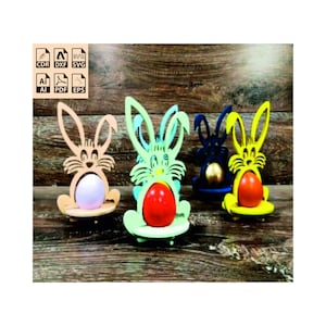 May include: Four wooden bunny egg holders, each painted a different colour: light brown, light green, dark blue, and yellow. Each bunny holds an egg, painted in a different colour: pink, red, gold, and yellow.