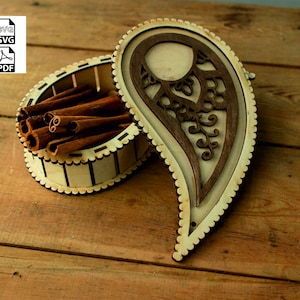 May include: A wooden box with a paisley design lid. The box is open and filled with cinnamon sticks.
