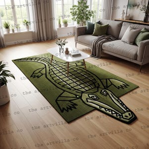 Puede incluir: Una alfombra rectangular verde con un gran diseño de caimán estilizado en negro. La alfombra está colocada sobre un suelo de madera en un salón, con un sofá, una mesa de centro y luz natural de una ventana.