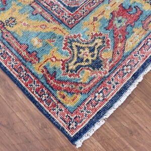 May include: Close-up of a blue, red, and yellow patterned rug with a fringed edge. The rug has a traditional design with intricate details.