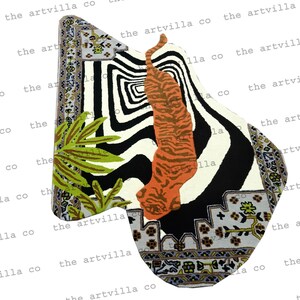 May include: A uniquely shaped rug with a tiger design. The rug features a zebra stripe pattern, an orange tiger, and a green leaf design. The rug has a decorative border with floral and geometric patterns. The text "the artvilla co" is repeated around the edge.