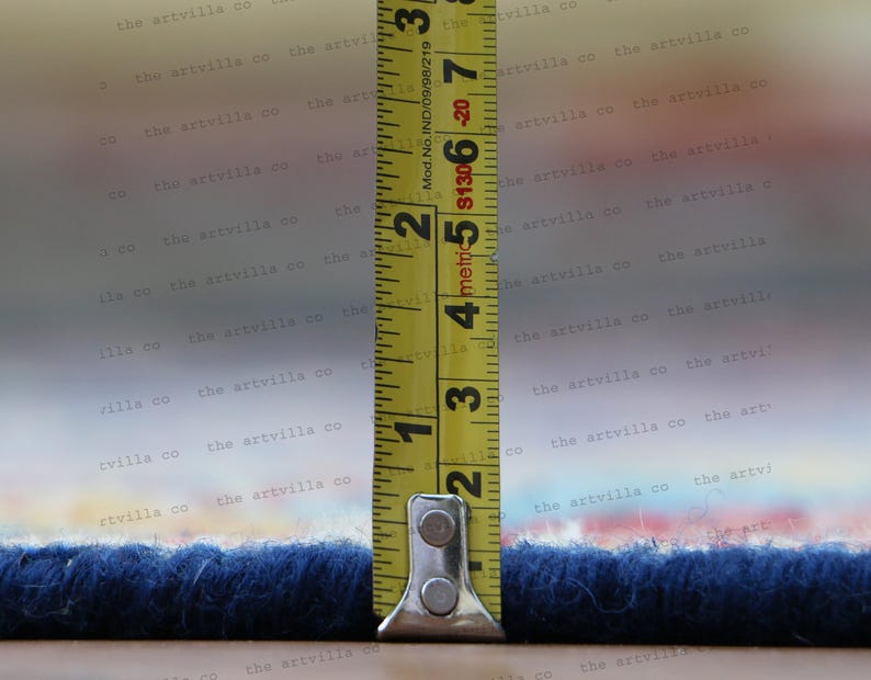 May include: A yellow measuring tape with black markings is extended to measure the width of a blue rug. The tape reads "metric 5 4 3 2 1" and "Mod. No. IND/09/98/219 $1306-20 7 3".