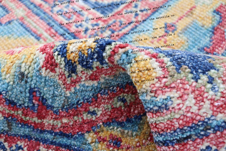 May include: Close-up of a colorful, textured rug with a repeating pattern. The rug is made of a soft, fuzzy material and has a variety of colors, including blue, pink, yellow, and white. The text "the artvilla co" is repeated throughout the image.