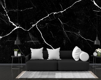 May include: A black sofa with white pillows sits in front of a black and white marble wall. Two black pendant lights hang from the ceiling. There are two small black side tables with plants and a clock on them.