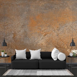 Könnte beinhalten: Ein schwarzes Sofa mit weißen Kissen steht vor einer Wand mit einer rostigen, strukturierten Oberfläche. Zwei schwarze Pendelleuchten hängen über dem Sofa, und zwei kleine Beistelltische mit Pflanzen und Uhren stehen auf beiden Seiten des Sofas.