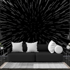 May include: A black sofa with three white pillows sits in front of a black wall with a white starburst pattern. There are two black end tables with plants and lamps on either side of the sofa.