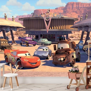 Op de afbeelding: Een kleurrijk behang met personages uit de animatiefilm Cars. De scène toont Bliksem McQueen, Takel, Sally en andere voertuigen voor Flo's V8 Cafe. De achtergrond toont een woestijnlandschap met een blauwe lucht.