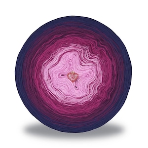 May include: A round ball of yarn with a gradient of colors, transitioning from a deep navy blue to shades of pink and white in the center. A small, heart-shaped charm is in the center. The yarn is likely for knitting or crochet projects.