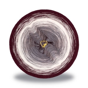 Op de afbeelding: Een bol garen in tinten van bordeauxrood, grijs en wit. Het garen is in een cirkelvorm gewikkeld met een gouden hartvormige hanger in het midden.