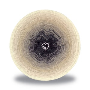 Può includere: Un gomitolo di filato in un gradiente di beige, marrone e nero. Il filato è avvolto in un cerchio e ha un piccolo ciondolo a forma di cuore argentato con strass al centro.
