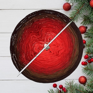 Könnte beinhalten: Ein großer, runder Wollknäuel mit einem Farbverlauf von Dunkelbraun zu Rot. Ein kleiner Anhänger ist am Garn befestigt. Das Bild ist mit Weihnachtsschmuck und Tannenzweigen dekoriert.