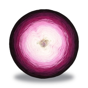 May include: A round ball of yarn with a gradient of colors, transitioning from dark purple to light pink and white in the center. A small, heart-shaped charm is placed in the center. This yarn is suitable for knitting and crochet projects.