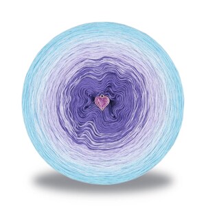 May include: A ball of yarn with a gradient of colors, transitioning from light blue to purple. A small, heart-shaped charm hangs in the center. The yarn is likely for knitting or crocheting projects.
