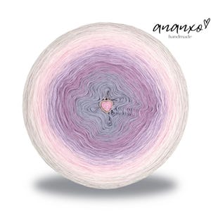 Puede incluir: Una bola redonda de hilo con un degradado de colores, incluyendo blanco, rosa, lavanda y gris. Un pequeño dije en forma de corazón está adjunto en el centro. El texto "ananxo handmade" está en la esquina superior derecha.