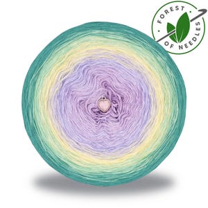 May include: A round ball of yarn with a gradient of colors, including teal, yellow, and lavender. A small, pink heart-shaped charm is attached to the center. The yarn is labeled "Forest of Needles."