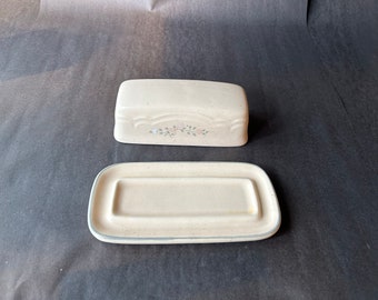 May include: A white ceramic butter dish with a floral design. The dish has a lid and a separate base.