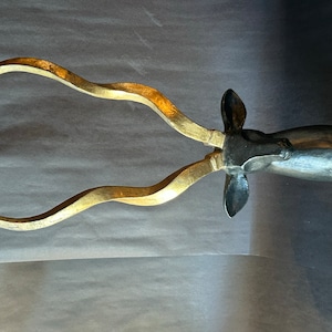 May include: A decorative wall hanging featuring a stylized antelope head. The sculpture has a dark gray body with gold-colored, curved horns. The horns have a textured appearance, adding visual interest to the piece.