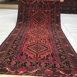 May include: A long, narrow rug with a traditional Persian design. The rug is primarily red and black with intricate geometric patterns and floral motifs. The rug has a fringe on both ends.