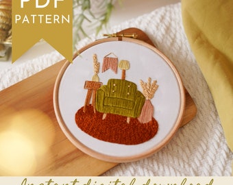以下が含まれることがあります： 居間のシーンを描いた刺繍フープアート。デザインには、緑のアームチェア、小さなテーブル、ランプ、装飾要素が含まれています。「PDF PATTERN」と「Instant digital download」の文字が見えます。刺繍は木製のフープにセットされています。