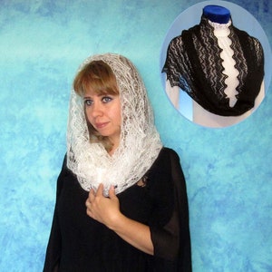 May include: A woman wearing a black dress and a white lace shawl. She is standing in front of a blue background.
