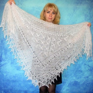 May include: A white lace shawl with a delicate pattern. The shawl is being held by a person and is draped over their shoulders.