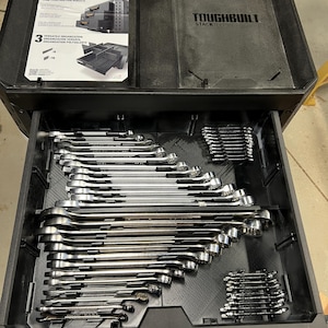 Könnte beinhalten: Schwarze Toughbuilt Stack Werkzeugkiste mit einer offenen Schublade, gefüllt mit einem Satz glänzender Schraubenschlüssel. Die Oberseite der Box hat ein Diagramm und die Worte "TOUGHBUILT STACK".