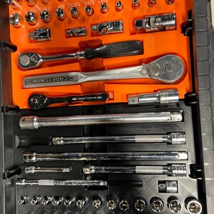 May include: A black toolbox with an orange interior, filled with a variety of chrome sockets, ratchets, and extensions. The Craftsman brand is visible on some of the tools. Sockets are labeled with fractional inch measurements.