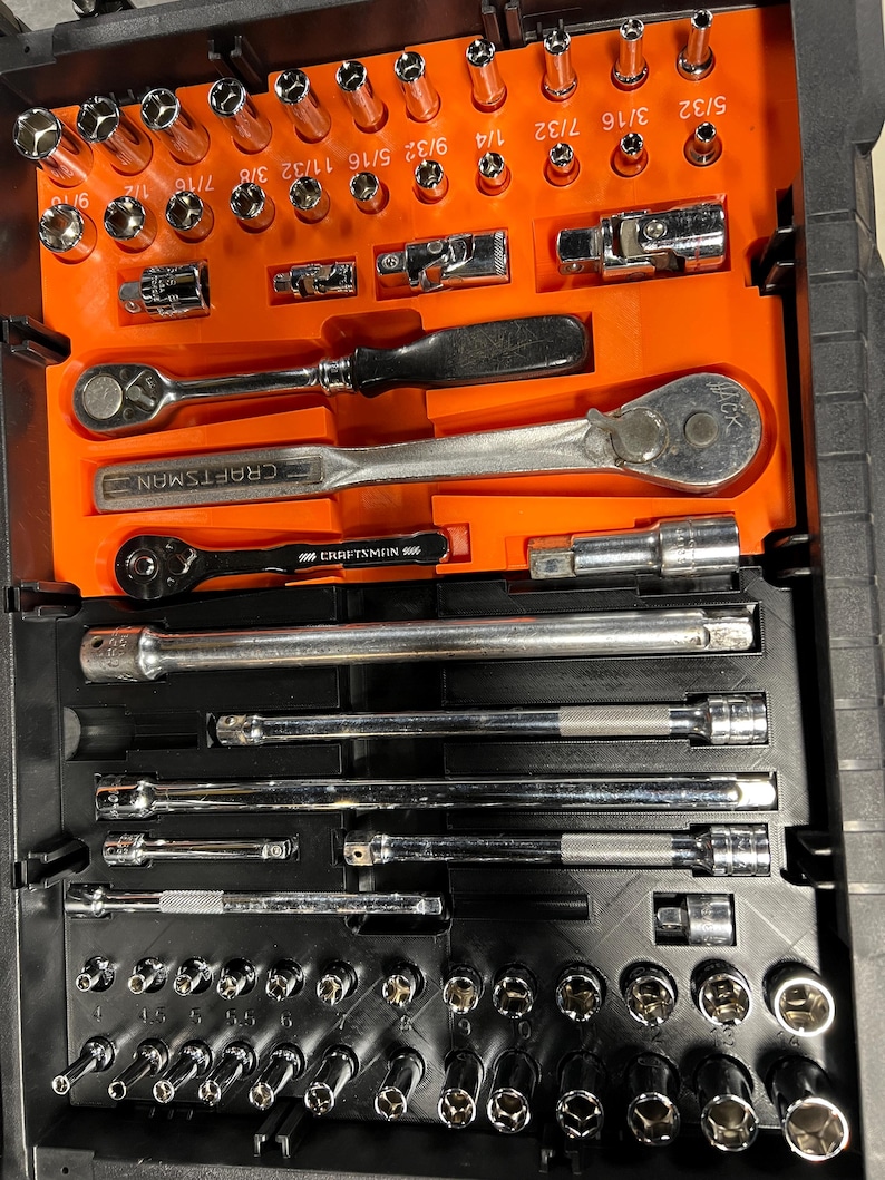 May include: A black toolbox with an orange interior, filled with a variety of chrome sockets, ratchets, and extensions. The Craftsman brand is visible on some of the tools. Sockets are labeled with fractional inch measurements.