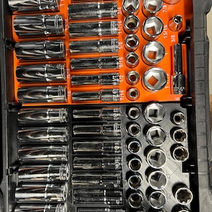 May include: A set of chrome sockets and extensions arranged in a black and orange storage case. The sockets are various sizes, including 1/2, 5/8, 3/4, and 7/8 inch. The case is organized with labeled slots for each tool, providing a clear view of the contents.