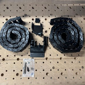Puede incluir: Cadenas de cables de plástico negro y componentes relacionados dispuestos sobre una superficie de madera. Las cadenas están enrolladas, con conectores y sujetadores. Los artículos son para una máquina CNC.