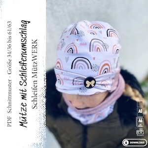 Könnte beinhalten: Eine weiße Mütze mit Regenbogenmuster und einer rosa Schleife. Die Mütze ist für die Größen 34/36 bis 61/63 geeignet. Der Text "Mütze mit Schleifenumschlag" ist in Schwarz auf weißem Hintergrund geschrieben.