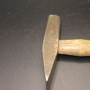 May include: A metal hammer with a wooden handle. The hammer head is a dull silver color, and the handle is a light brown. The hammer is designed for striking and shaping materials.