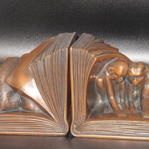 May include: Bronze-colored bookends featuring a sculpted design of monkeys peering out from behind open books. The bookends are detailed with textured pages and monkey figures, adding a unique touch to any bookshelf.