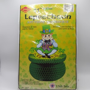May include: A Beistle brand Leprechaun art-tissue centerpiece in original packaging. The yellow package features a leprechaun sitting on a green honeycomb pot filled with gold coins. Text includes Leprechaun Art-Tissue Centerpiece and Metric 28 cm.