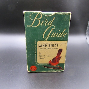 May include: A vintage green "Bird Guide" book with gold lettering and a red bird illustration. The book, titled "Land Birds East of the Rockies," features text including the author's name and the number of species.