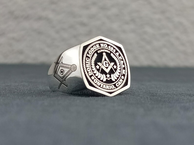 Puede incluir: Anillo mas&oacute;nico de plata con una incrustaci&oacute;n de esmalte negro que presenta una br&uacute;jula y una escuadra, rodeados por una corona y el texto "Doric Lodge No. 484 A.F. & A.M. Ontario, Can."