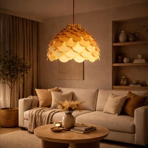 Può includere: Una lampada a sospensione decorativa dorata, a forma di cupola, è appesa a un cavo rosso. La lampada è composta da elementi circolari sovrapposti. L'apparecchio illumina un soggiorno con un divano beige, cuscini e un tavolino rotondo in legno.