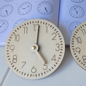 Könnte beinhalten: Zwei Holzuhren mit schwarzen Zahlen und Zeigern. Die Uhr links zeigt 12:00 Uhr und die Uhr rechts zeigt 1:00 Uhr.