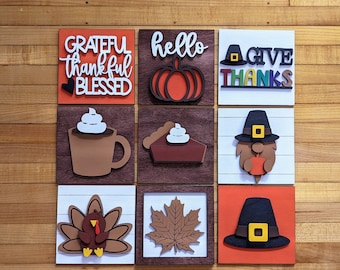 Puede incluir: Nueve letreros de madera con temática otoñal. Los letreros presentan frases como "Grateful Thankful Blessed", "Hello", "Give Thanks", e imágenes de una calabaza, un pastel, un gnomo, un pavo y una hoja.
