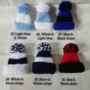May include: Six knitted baby hats with pom-poms in various color combinations: light blue and white, white and light blue, blue and black stripe, white and navy stripe, navy and white stripe, and red and black.